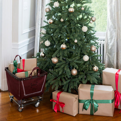 Decorated Christmas tree with presents and a cart in a room with large windows.