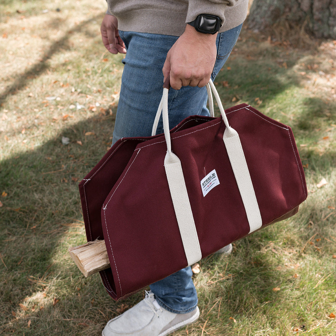 Person holding a auburn log carrier with white handles outdoors.