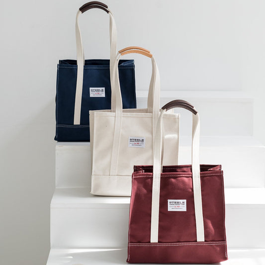 three tote bags in navy, beige, and red on a white surface with a light gray background.