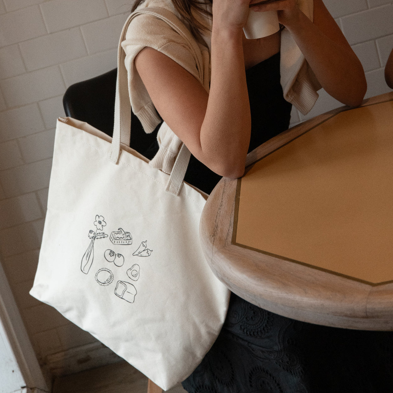 Woman sitting in a bathroom holding a phone, with a tote bag on her lap.