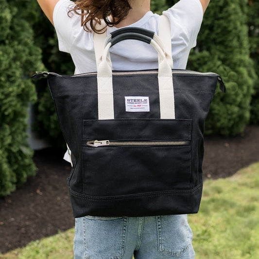 Person wearing a black tote bag with white straps outdoors