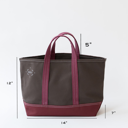 A dark brown and burgundy tote bag with white stitching, shown with dimension lines and labels indicating its measurements: 12 inches tall, 14 inches wide, and 7 inches deep.