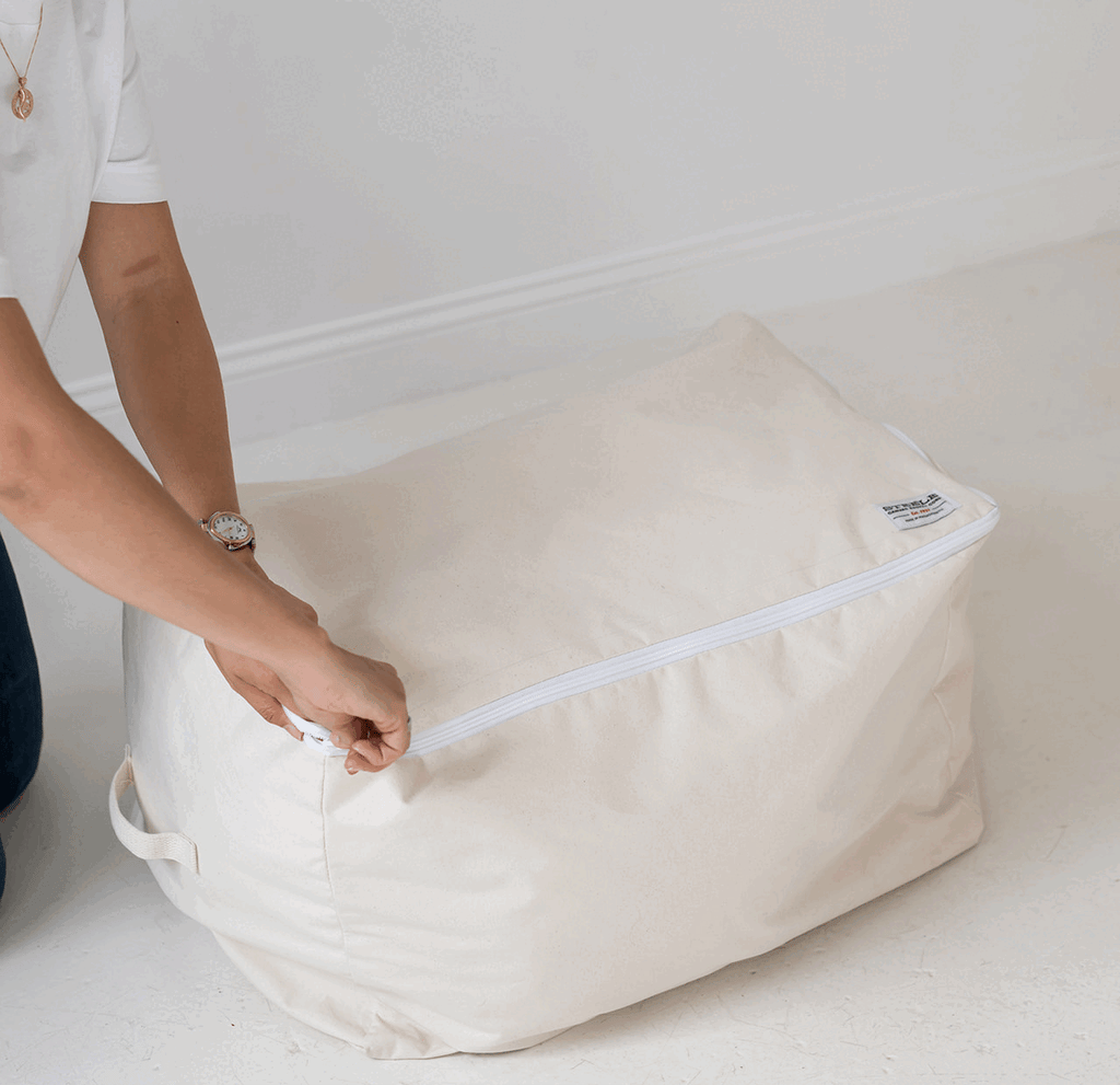 Person zipping a large beige storage bag on a light background