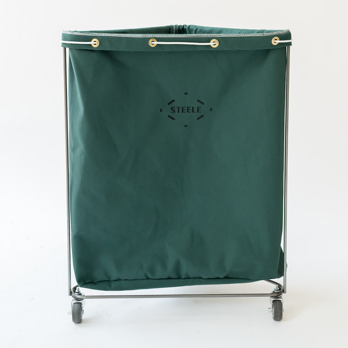 A dark green canvas laundry hamper with a metal frame and caster wheels, featuring the brand name 'STEELE' printed on the front, set against a plain white background.