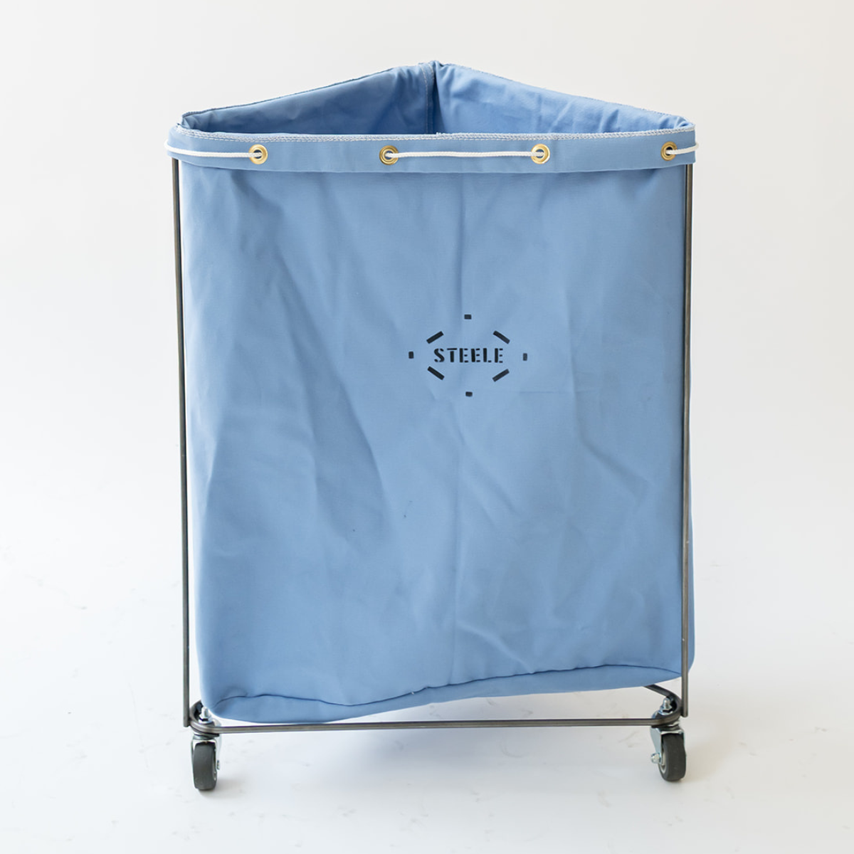 A light blue fabric laundry hamper with a steel frame and caster wheels, featuring a black 'STEELE' logo printed on the front.