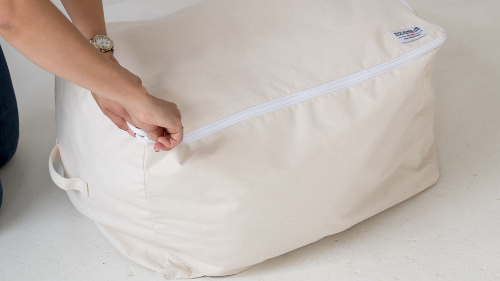 Person zipping a large beige storage bag on a light background